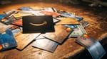 Amazon black card with smile logo dominates scattered credit cards on worn wooden desk.