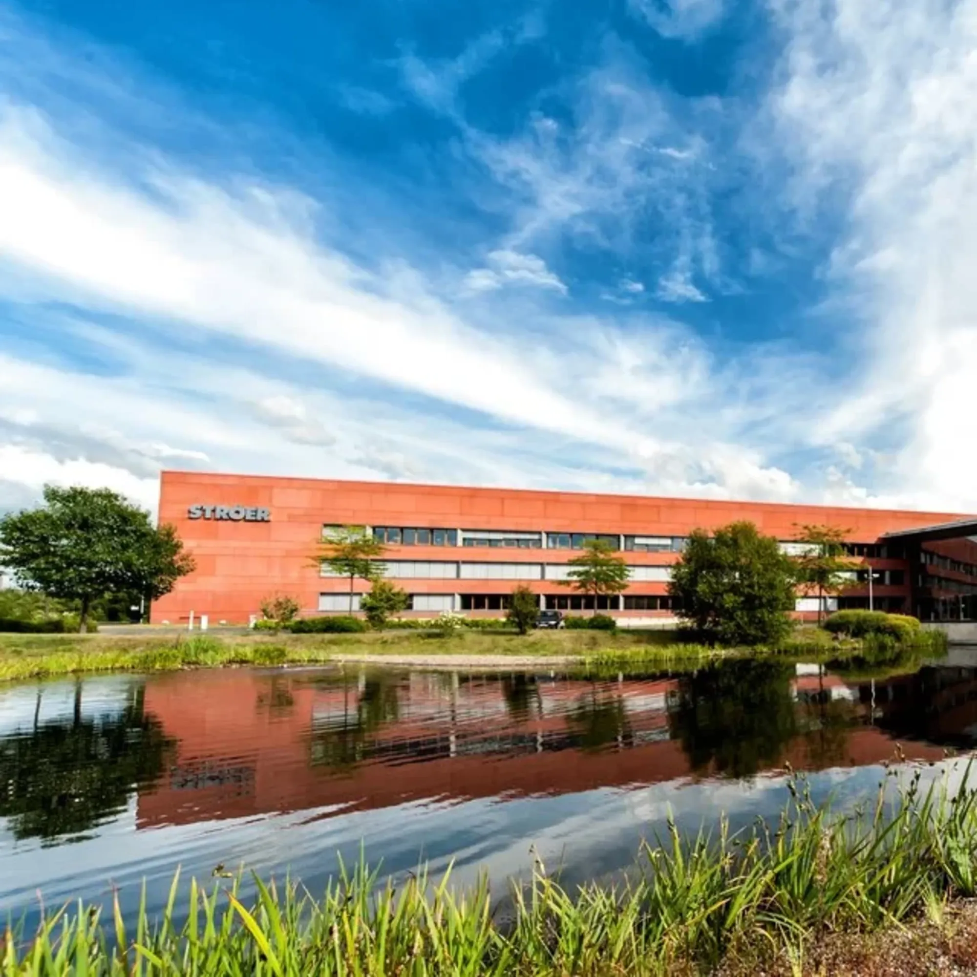 Ströer headquarters building reflects in lake under dramatic sky, showcasing German media firm's modern campus