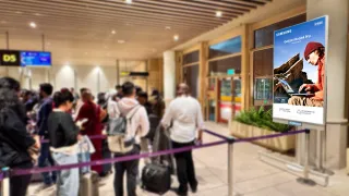 Digital advertising screen displays Samsung Galaxy Book4 Pro ad to queuing passengers at airport terminal.