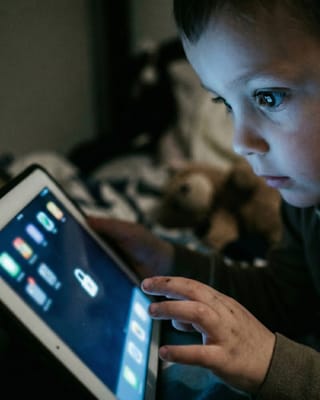 Child browsing apps on tablet in the dark, unprotected from harmful online content.