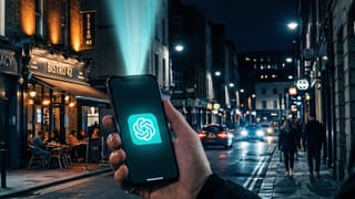 ChatGPT app glowing on a smartphone at night, illuminating a city street with local businesses nearby.