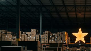 A single glowing orange star inside a dark Amazon warehouse filled with stacked boxes.