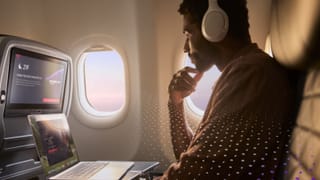 A passenger uses a laptop on a Delta flight with Amazon Leo Wi-Fi, seat 21F visible on the seatback screen.