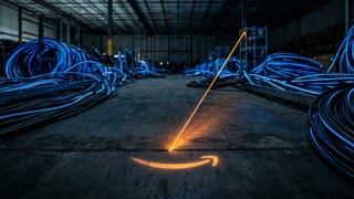 A single amber thread meets the Amazon smile on a dark warehouse floor, dwarfed by blue cables.