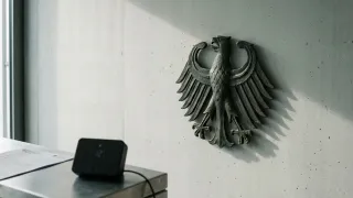 German federal eagle on concrete wall beside a connected smart thermostat and printed document
