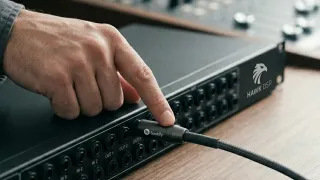 Hand connects a Spotify-branded cable into a Hawk DSP audio patchbay on a wooden desk