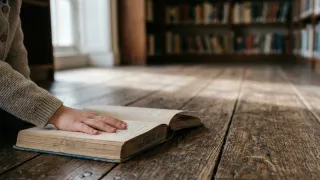 Child's hand resting on an open book on a wooden library floor, soft window light