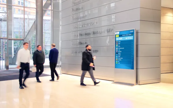 DOOH screen shows status updates in modern office lobby as professionals walk past