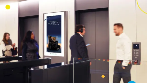 Digital screen displays luxury travel ad in office lobby as business professionals pass by elevators during work hours.