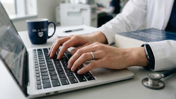 Physician typing health content on laptop beside stethoscope, representing telehealth EEAT signals.