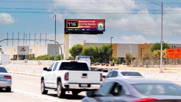 Clear Channel digital billboard on Phoenix highway displaying 116F heat alert and 2-1-1 hotline