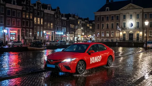 Red Yango taxi driving at night through rain-slicked Amsterdam streets near a canal.